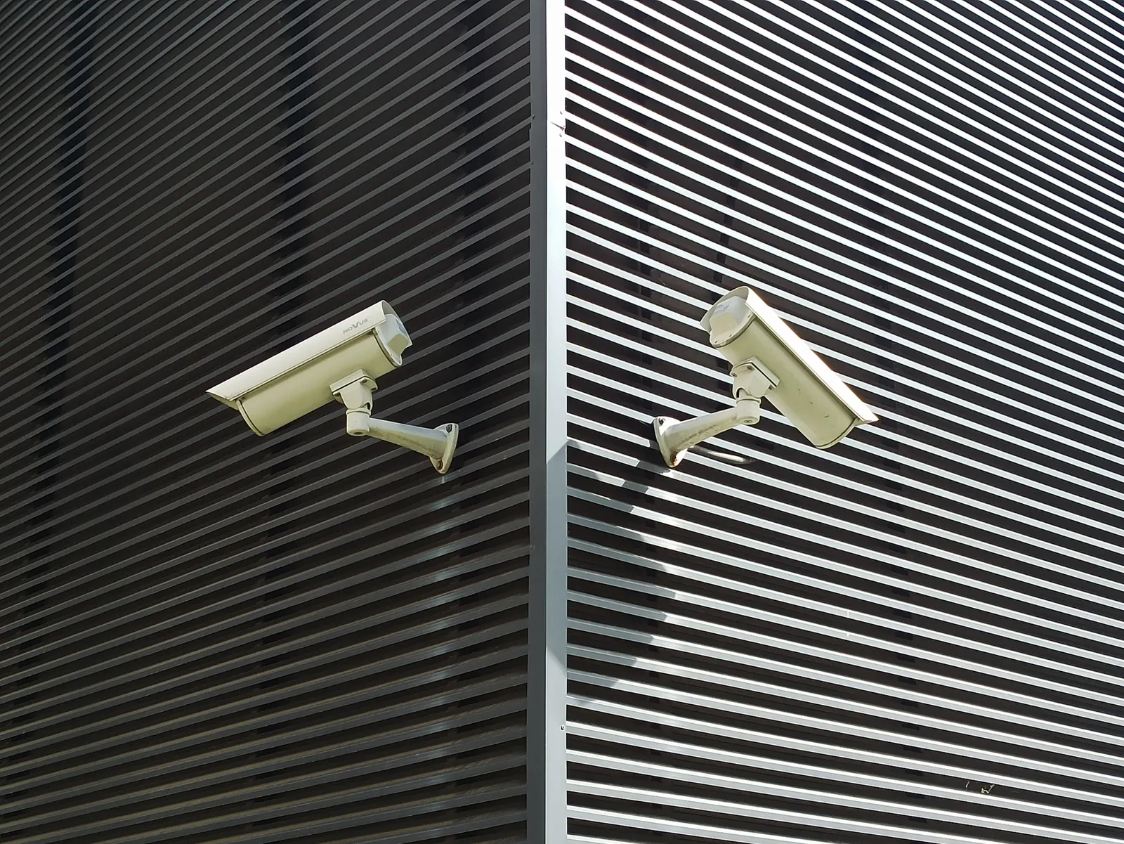 Two bullet CCTV cameras fixed to a louvred building facade