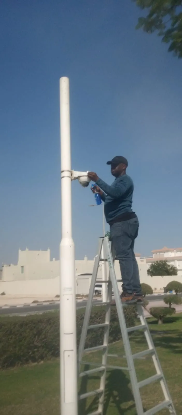 Manifeso technician on a ladder fixing a camera to a pole in the park